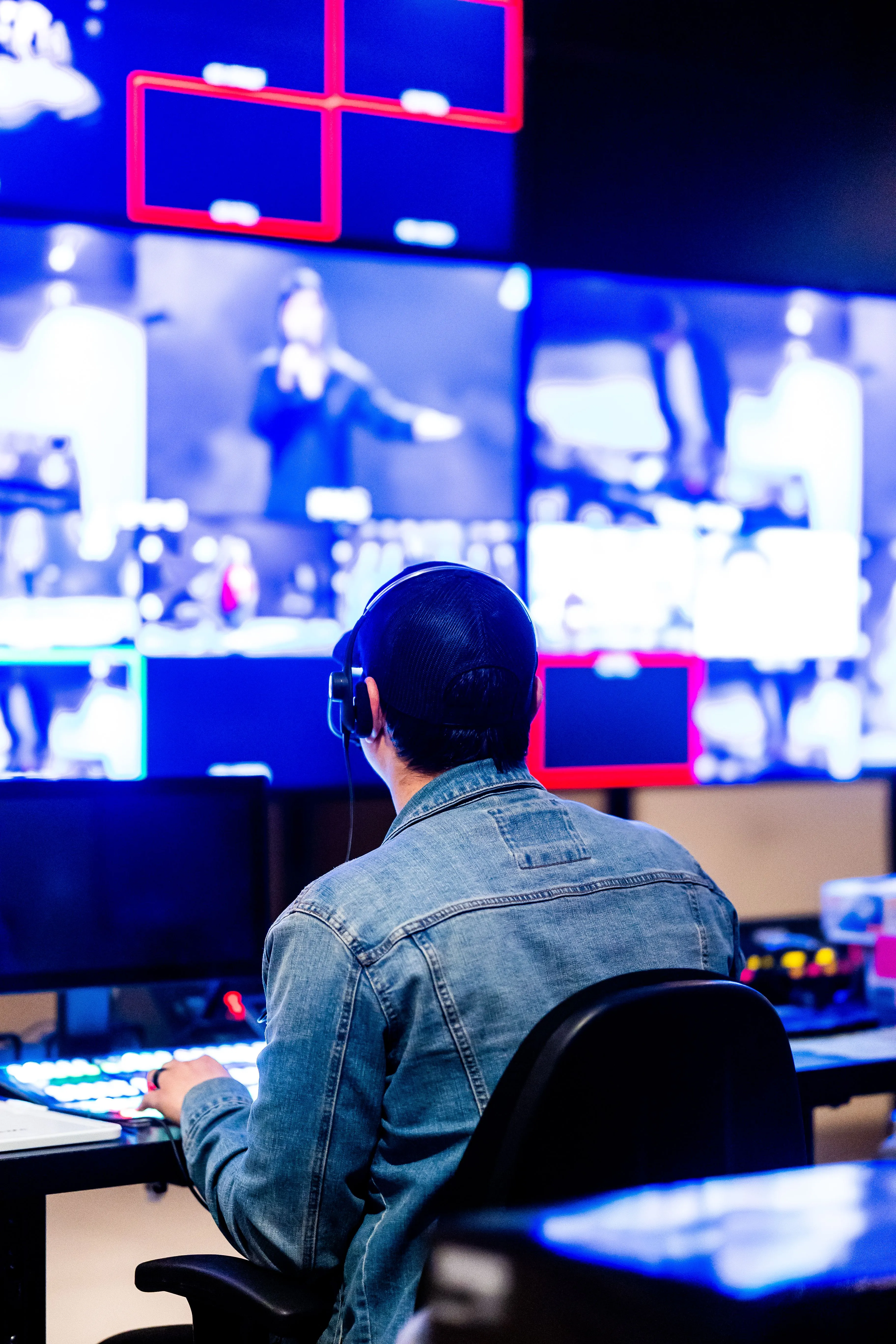 An operator at a broadcast control desk facing a wall of monitors